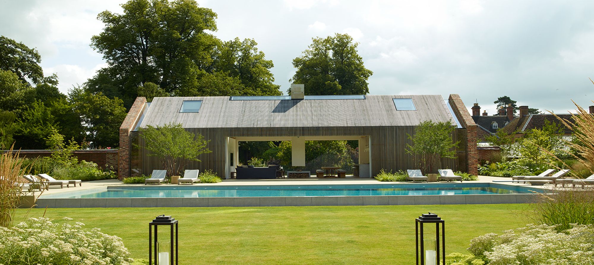 a poolhouse overlooks a swimming pool in the cotswolds